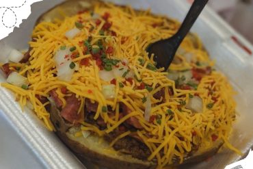 Cheeseburger with shredded cheddar, lettuce, onions, and seasoned beef in a foam container for travel | delicious cheeseburger loaded with toppings and cheese, perfect for on-the-go meals at travel destinations | close-up of cheeseburger with fresh toppings, melted cheese, and seasoned beef in disposable container, ideal for street food or travel snacks | relevance: Yes.