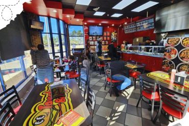 Bright fast-food restaurant interior with customers ordering and dining, featuring colorful branding, modern decor, large menu screens, and natural light from large windows, ideal for quick service dining experiences.