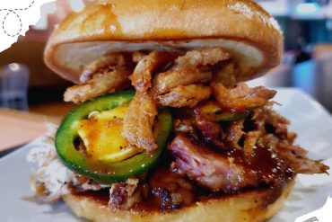 Crispy fried chicken sandwich with jalapeño peppers and barbecue sauce, served on a brioche bun, showcasing American comfort food and delicious travel-inspired cuisine.