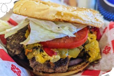Beef burger with lettuce, tomato, cheese, and grilled patty on toasted bun, fast food meal, vibrant and delicious American-style burger for travel and food lovers.