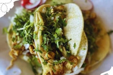 Fresh Mexican street taco filled with fried chicken, fresh chopped herbs, and shredded lettuce, served on a soft corn tortilla, representing vibrant flavors and authentic cuisine.