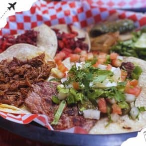 Slow-cooked taco meat, fresh salsa, grilled vegetables, and lime wedges served on traditional street-style tacos, representing authentic Mexican cuisine.