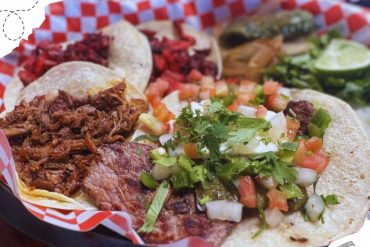 Slow-cooked taco meat, fresh salsa, grilled vegetables, and lime wedges served on traditional street-style tacos, representing authentic Mexican cuisine.