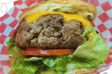 Juicy burger with crispy lettuce, fresh tomato slices, melted cheese, and a flavorful beef patty served in a casual outdoor setting. Perfect for food lovers and travel enthusiasts seeking local culinary delights.