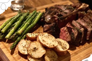 Succulent grilled steak with roasted garlic potatoes and fresh asparagus on a wooden platter, perfect for a delicious travel-inspired dining experience at Go To Destinations.