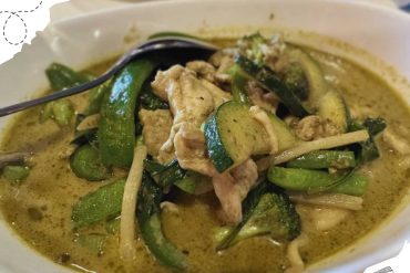 Steamed green curry with chicken and zucchini in a creamy yellow sauce, served in a white bowl, highlighting Thai cuisine, travel, and food culture.
