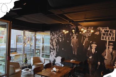 Vintage-themed cafe interior with modern seating and historic protest mural, cozy atmosphere, large windows for natural light, perfect for relaxing or casual gatherings.