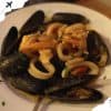 Steamed mussels with pasta and seafood, served on a white plate, garnished with herbs, showcasing delicious international cuisine, perfect for travel food experiences, Go To Destinations image.