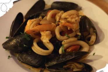 Steamed mussels with pasta and seafood, served on a white plate, garnished with herbs, showcasing delicious international cuisine, perfect for travel food experiences, Go To Destinations image.