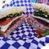 Crispy breakfast club sandwich with fresh vegetables and deli meats on checkered blue and white paper, ideal for travel and food lovers, showcasing delicious and portable meal options for destinations.