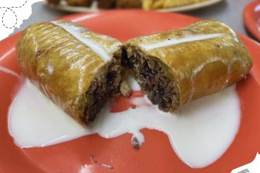 Savory Mexican beef tamale with rich meat filling, wrapped in corn husk, served with creamy sauce on orange plate. Perfect for authentic Mexican cuisine and travel food experiences.