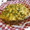 Crispy baked potato topped with melted cheese and chopped chives at a food festival.