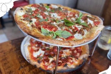 Freshly baked pizza with basil leaves on a two-tier stand at a restaurant, showcasing delicious Italian cuisine and travel food experiences.