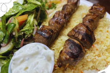 Skewered grilled meat served with rice, fresh salad, and yogurt sauce, showcasing Middle Eastern cuisine. Perfect for food lovers seeking authentic flavors and diverse culinary experiences.