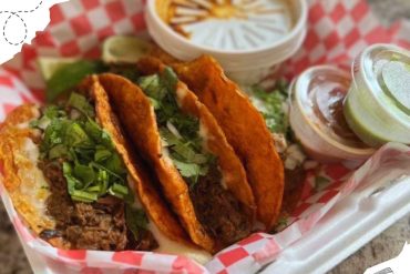 Crispy beef tacos with fresh cilantro and lime wedges, served with salsa and sauces, on red checkered paper tray - Mexican street food, authentic flavors, delicious and savory meal, vibrant presentation.