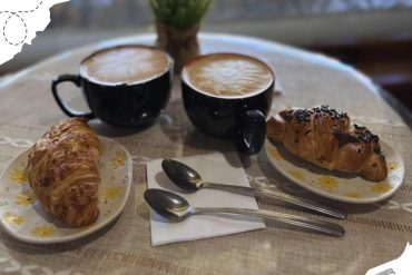 Coffee cups with cappuccinos and croissants on a table in a cozy cafe, perfect for breakfast or brunch, scenic window view, travel destination, café ambiance, comfort, and delicious pastries, travel and hospitality concept.