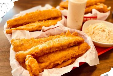 Crispy fried fish fillets served with coleslaw, tartar sauce, and extra fish in a basket at a casual seafood restaurant. Perfect for a delicious seafood meal while exploring new destinations.