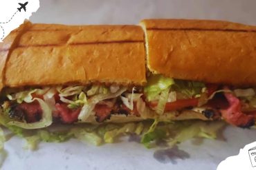 Cuban sandwich with crispy bread, fresh lettuce, tomato, ham, roast pork, and melted cheese, served as a popular and delicious street food option in Cuba.