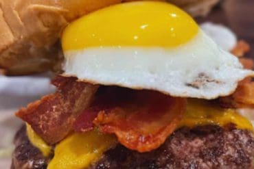 Juicy cheeseburger with crispy bacon, fried egg, fresh lettuce, and melted cheddar cheese on a toasted bun, perfect for burger lovers and food enthusiasts exploring delicious dining destinations.