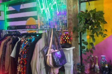 Vibrant thrift store interior with colorful neon sign, clothing rack, and vintage decor highlighting eclectic fashion shopping experience.