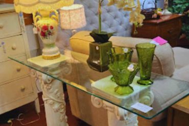 Ornate vintage lamp and glass table with decorative green glasses in cozy rustic living room.
