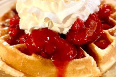 Warm waffle topped with fresh strawberries and whipped cream, served on a rustic plate for a delicious breakfast or dessert experience. Perfect for exploring delicious destinations and culinary adventures.