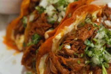 Tender shredded beef tacos topped with fresh cilantro and diced onions, served with a side of flavorful, spicy salsa; perfect for Mexican cuisine lovers.