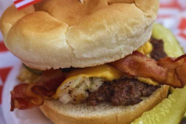 American cheeseburger with bacon on a soft bun, topped with lettuce and pickles, served with a small American flag. Perfect for travelers exploring US destinations and enjoying classic American cuisine.