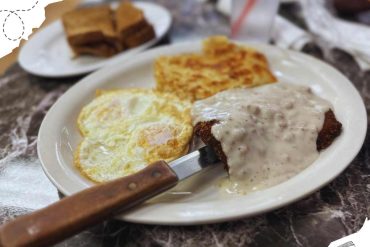 Fried steak with mushroom gravy, sunny side up eggs, hash browns, and toast served on a white plate. Classic comfort breakfast dish enjoyed at a local restaurant.