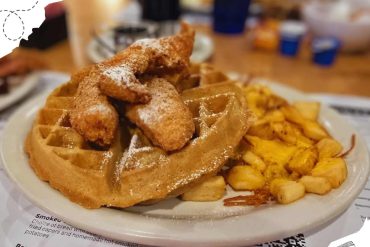 Waffles with fried chicken and hash browns served on a breakfast plate at a diner, showcasing classic American breakfast foods.