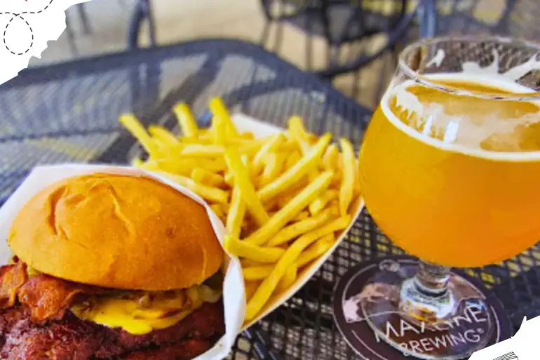A bacon cheeseburger with a side of French fries and an orange alcoholic beverage in a glass.
