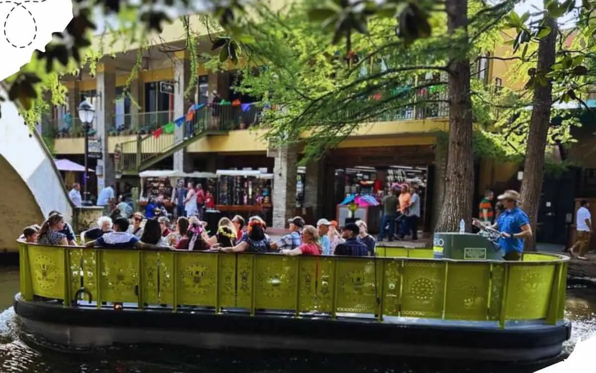 Riverboat cruise with tourists enjoying a scenic ride through a charming urban area surrounded by trees and colorful buildings, perfect for sightseeing and exploring city attractions.