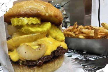 Golden cheeseburger with pickles and grilled onions served with crispy French fries, perfect for travel food lovers exploring new destinations.