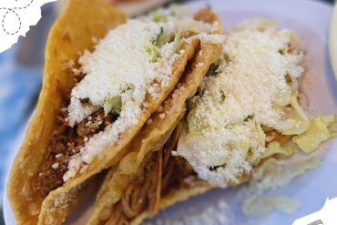 Soft-shell beef tacos with shredded beef, lettuce, cheese, and toppings, served on a white plate. Perfect for authentic Mexican cuisine, street food, and travel memories.