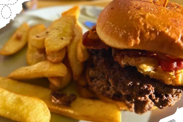 A burger with bacon in it and thick cut French fries on the side.