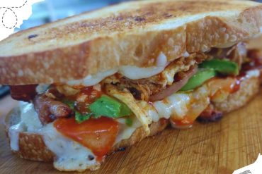 Crispy breakfast sandwich with egg, bacon, and vegetables on toasted bread, travel-themed background, food travel, delicious breakfast, food photography.