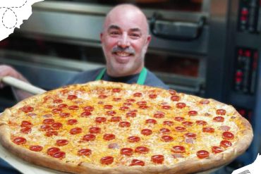 Fresh homemade pepperoni pizza served by smiling chef in a pizzeria.