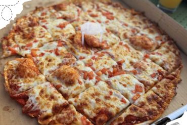 Oved cheese pizza with diced tomatoes in a cardboard box, close-up, delicious fast food meal, cheesy pizza slice with crispy crust, popular travel food at destinations, pizza delivery, comfort food, casual dining, food photography, American cuisine.
