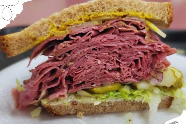 Tender corned beef sandwich with shredded meat, lettuce, pickles, and mustard on whole grain bread. Perfect for a hearty meal or travel snack.