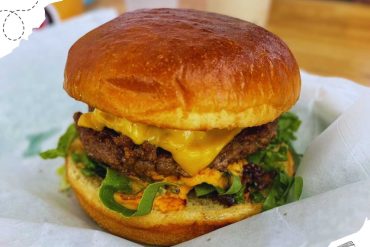 Cheeseburger with melted cheddar cheese, fresh lettuce, and a toasted bun, served on white parchment paper in a casual dining setting, perfect for travelers seeking local American cuisine.