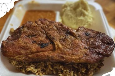 Grilled jerk chicken thigh served with mashed potatoes, gravy, and rice and peas on a takeout tray, showcasing Caribbean cuisine and authentic flavorful comfort food.