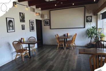 Modern cozy cafe interior with wooden tables, framed black-and-white photos, large window with natural light, and potted plant, perfect for relaxing or casual meetings.