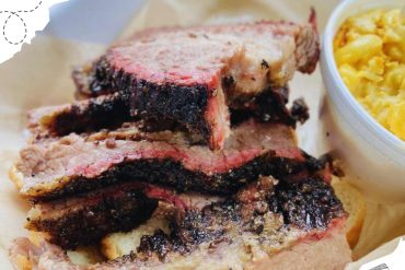 Thinly sliced, perfectly cooked, juicy Texas BBQ brisket with a smoky bark on a bun with a side of creamy mac and cheese, ideal for food lovers seeking authentic Southern barbecue experiences.