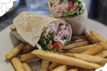 Fresh turkey wrap with lettuce, tomatoes, and cheese served with crispy French fries on a white plate, perfect for travel food lovers exploring diverse cuisine around the world.