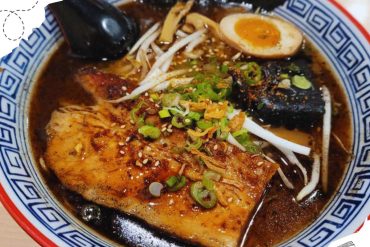 Spicy ramen bowl with fish, vegetables, soft-boiled egg, and green onions in a traditional patterned bowl, highlighting flavorful Asian cuisine for travel and food enthusiasts.