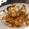 Delicious waffle with caramel sauce, whipped cream, pecans, and ice cream on a white plate, showcasing a sweet dessert from popular travel destinations, perfect for food lovers and travelers.