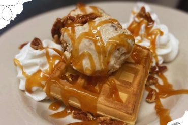Delicious waffle with caramel sauce, whipped cream, pecans, and ice cream on a white plate, showcasing a sweet dessert from popular travel destinations, perfect for food lovers and travelers.