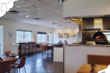 Modern restaurant interior with wood-fired pizza oven, cozy dining area, and large windows providing natural light, ideal for travelers seeking delicious meals and a comfortable ambiance.