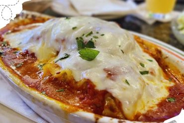 Creamy baked lasagna with melted cheese, tomato sauce, and fresh herbs served in a ceramic dish. Perfect comfort food for travel-inspired culinary experiences and Italian cuisine lovers.