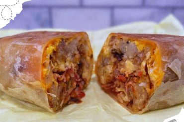 Cheesy beef burrito sliced in half showing seasoned meat, melted cheese, and vegetables inside, served on parchment paper against a blurred background.